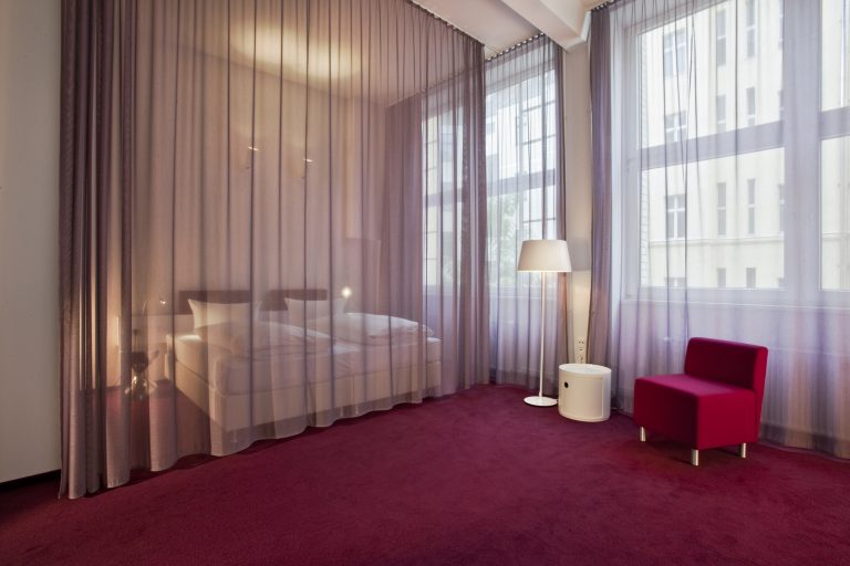 Boden, Möbel und Vorhänge in dunklem Magentarot sind die kräftigen Stilmittel der Hotelzimmer mit hohen Decken und den rauen Oberflächen der alten Stahlsteindecken.
